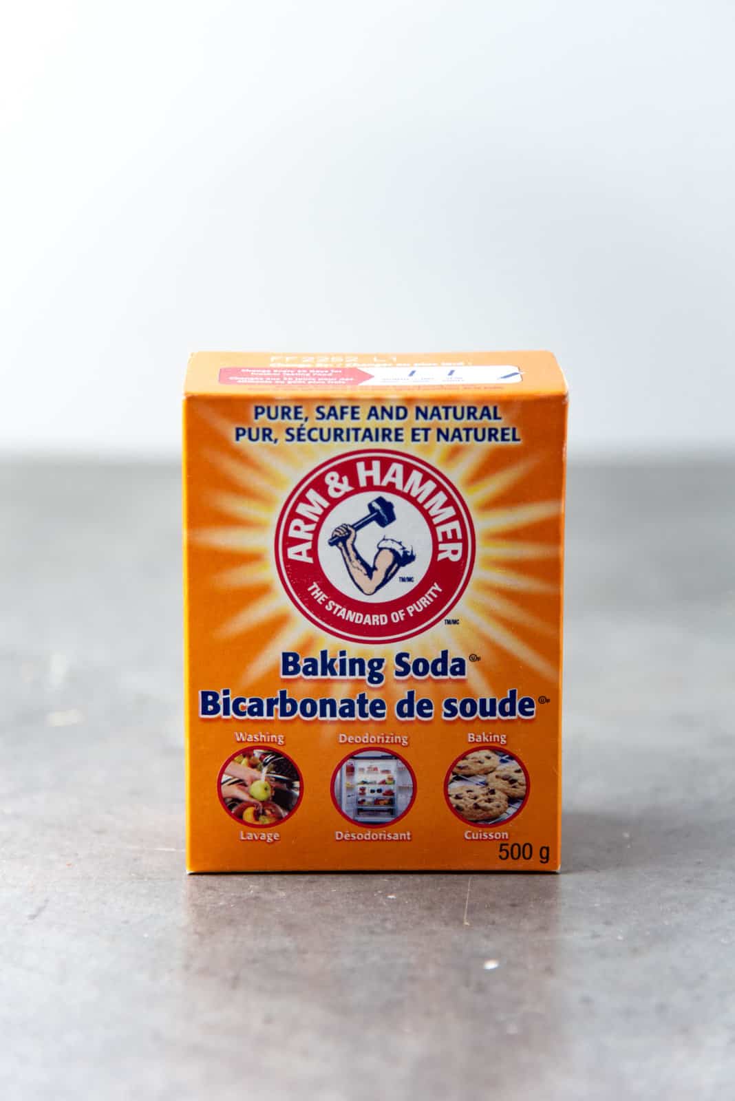 An orange box of baking soda on a grey surface.