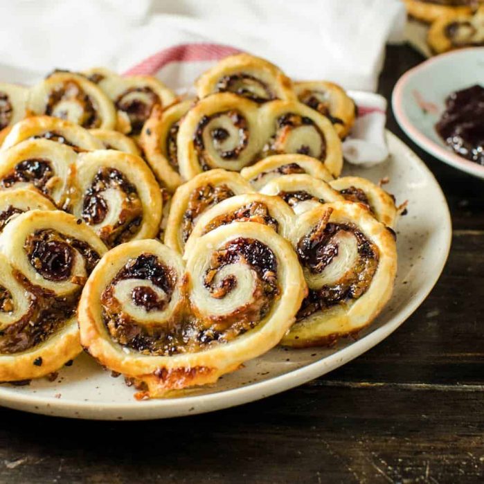 A plateful of puff pastry savory palmiers showing the berry jam and cheese filling on top.