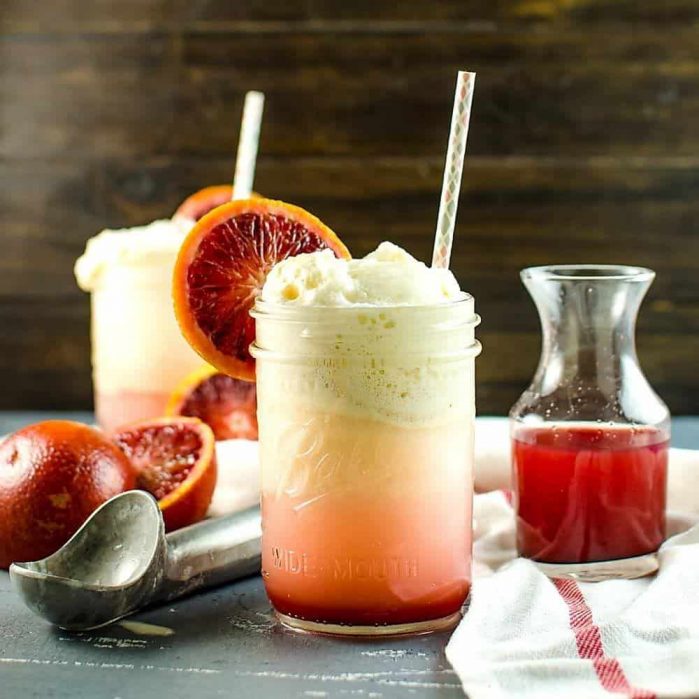 Blood orange soda float served with vanilla ice cream in a glass jar, and blood orange syrup in the background.