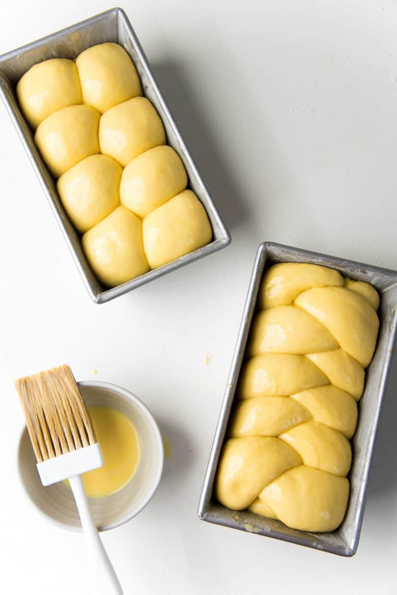Two unbaked brioche bread loaves in pans, one is braided and other is shaped in the Nantaise method.