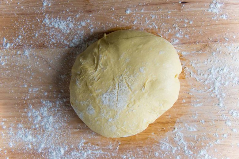 Shaped brioche dough sitting on a lightly floured wood work surface.