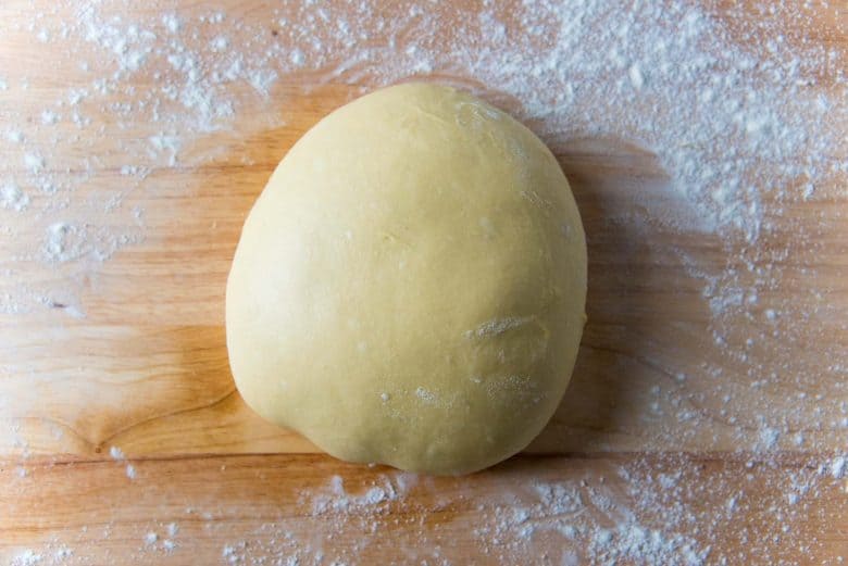 A smooth and shaped brioche dough ball on a lightly floured wood work surface.