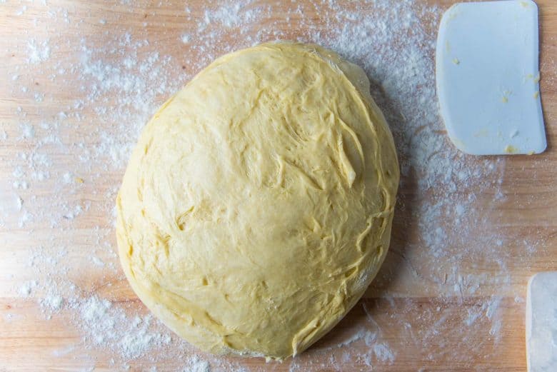 Dough on a lightly floured work surface with a flexible bowl scraper on the side.