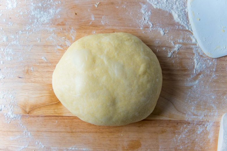 Smooth ball of brioche dough on a light floured wood work surface.