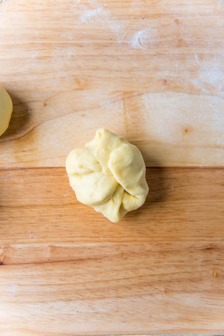 Shaping a dough portion by folding the edges towards the middle to form a dough ball.