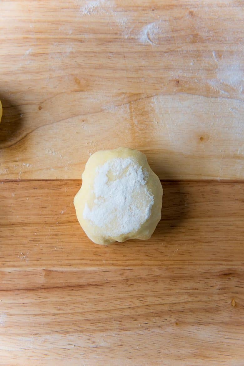 A small dough ball with a lightly floured surface on a wood block.