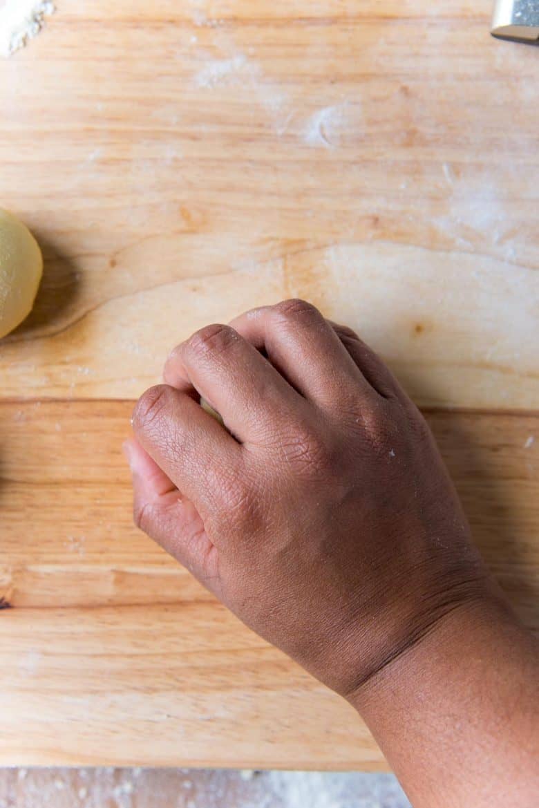 Rolling a dough portion with a cupped palm on a work surface to form a dough ball.