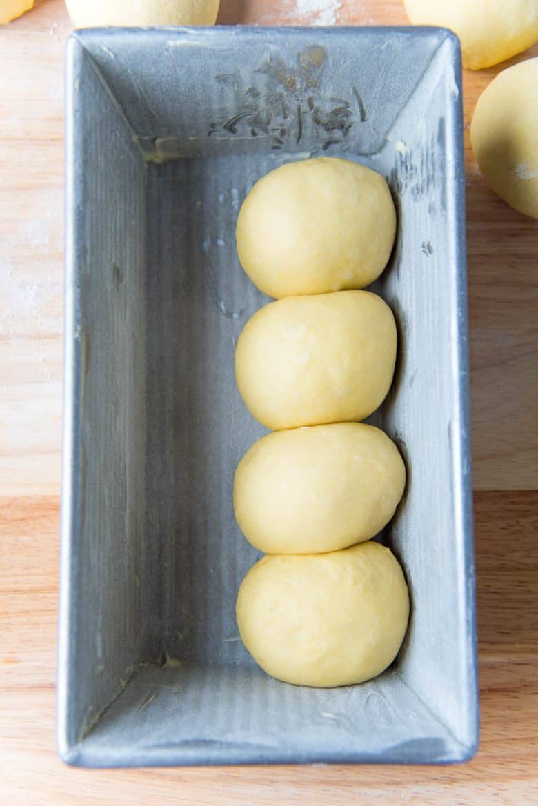 Four round dough balls placed in a row inside a metal loaf pan.
