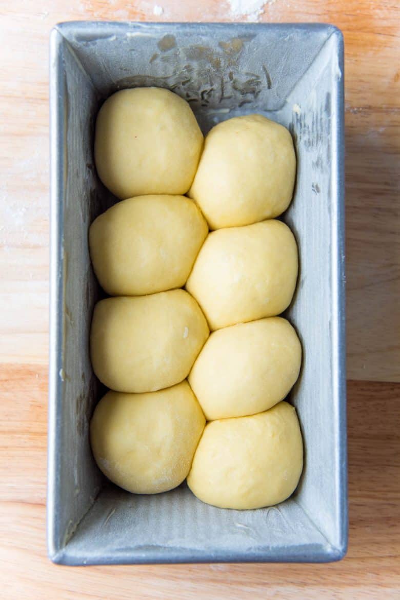 Eight round smooth dough balls placed inside a metal loaf pan to form a nantaise brioche loaf.