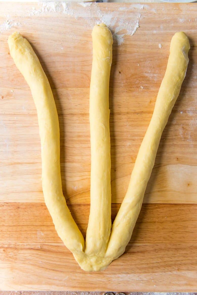 Three ropes of dough on a wood work surface with the ropes joined together on one end.