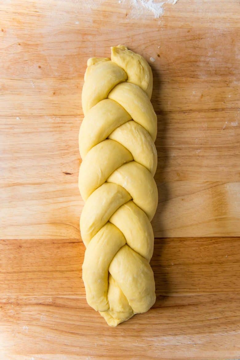 Braided brioche loaf dough on a wood work surface with the two ends pressed and sealed.