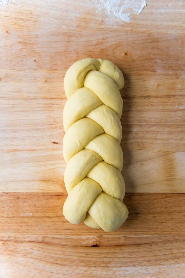 Braided brioche loaf dough on a wood work surface with two ends folded under the dough.