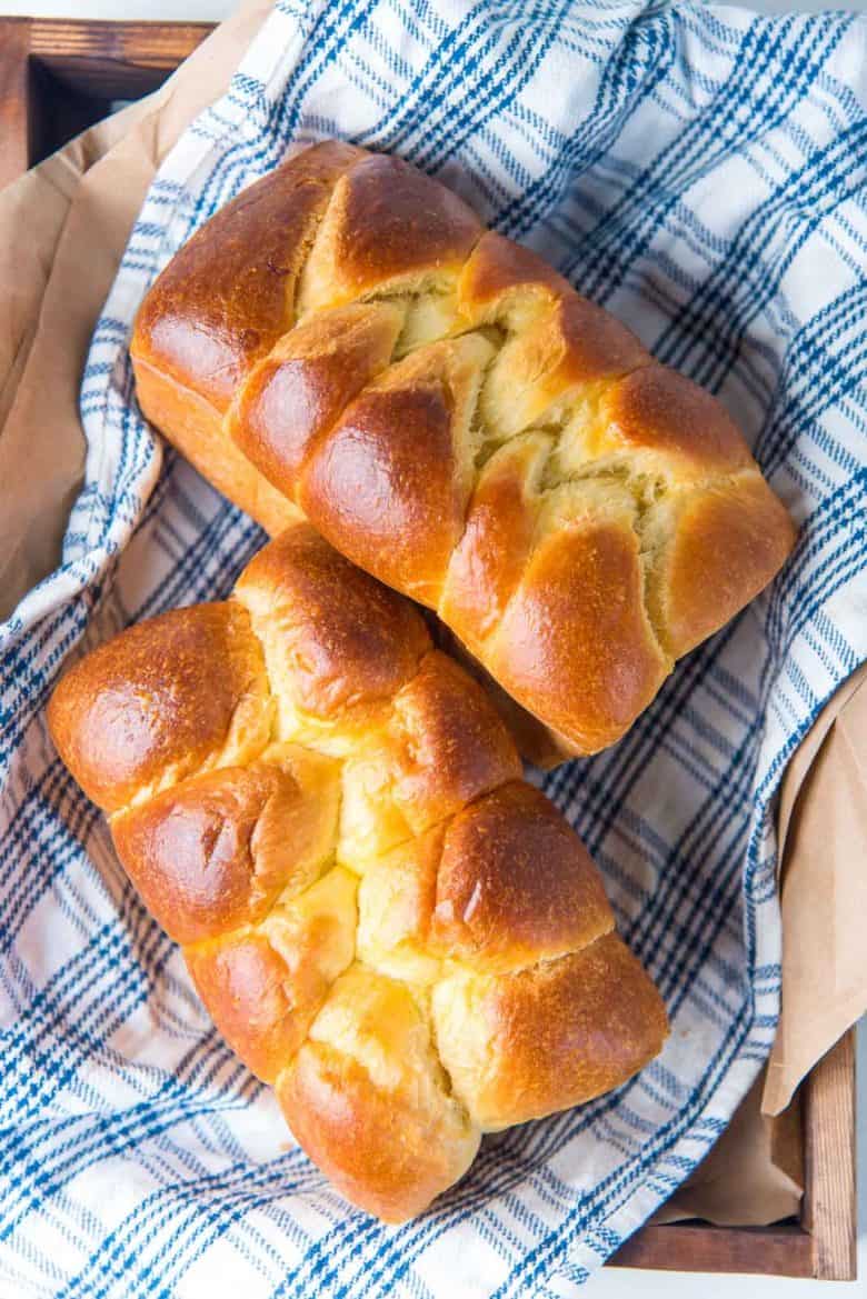Overhead view of two brioche loaves on a blue and white cloth napkin.