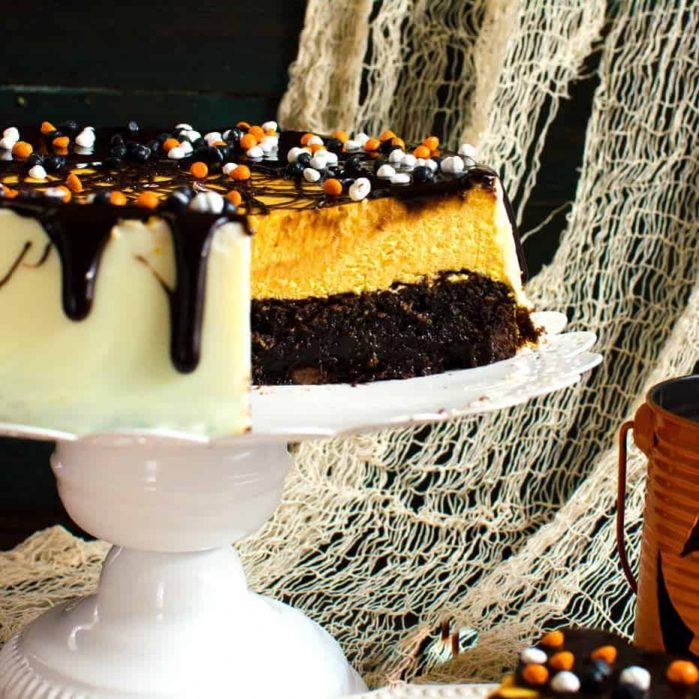 Brownie Bottom Pumpkin Cheesecake With Chocolate Fudge Sauce - A delicious combination of Fudgy brownies and creamy Pumpkin cheesecake in one dessert! Dress it up for Halloween or keep it simple to celebrate Thanksgiving or Fall. A great twist on Brownie Bottom Cheesecake with Fall flavors and Halloween cheer!