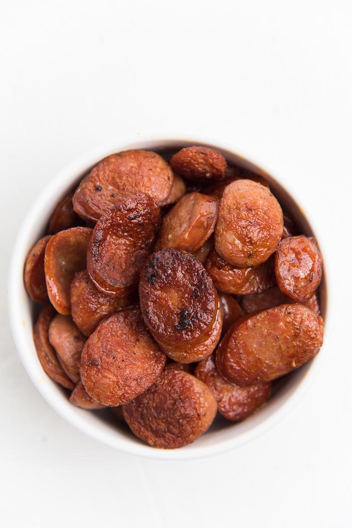 Pan fried andouille sausage slices in a white bowl on a white background.