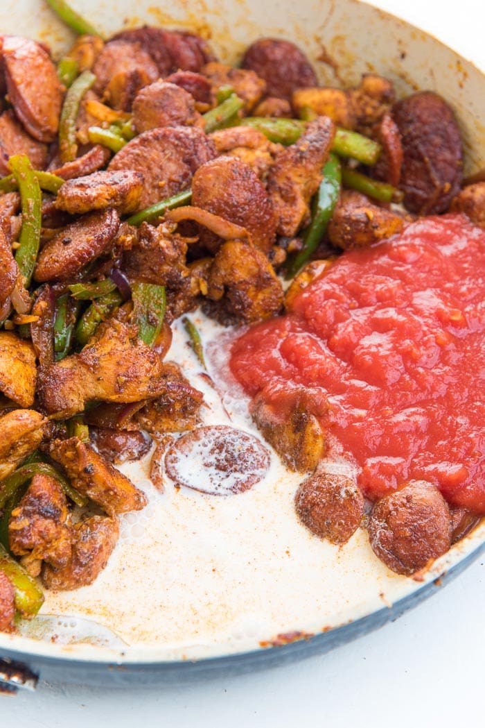 Adding tomato and cream to make the cajun pasta sauce in a large pan.