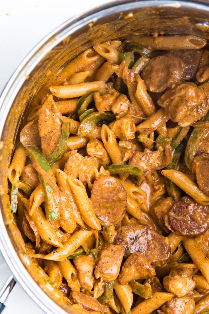 Penne pasta mixed into the cajun chicken and sausage in a pot.