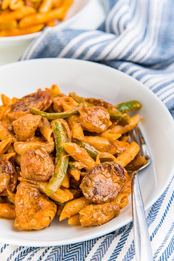 Creamy cajun chicken pasta served in a white bowl with a blue and white striped napkin in the background.