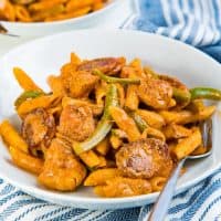 Cajun chicken and sausage pasta served on a white plate with a fork.