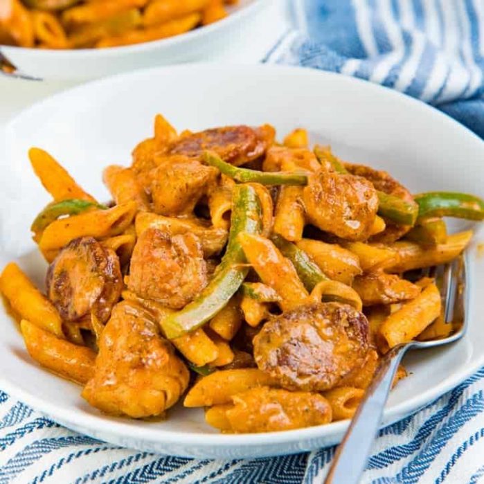 Cajun chicken and sausage pasta served on a white plate with a fork.