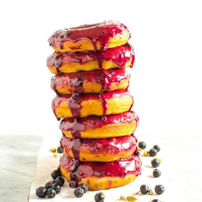 A tall stack of blueberry glazed doughnuts on a table with lots of blueberries around it.