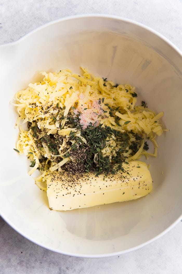 Recipe process for making thyme and cheddar cheese cookies - Butter, cheese and spices in a white bowl