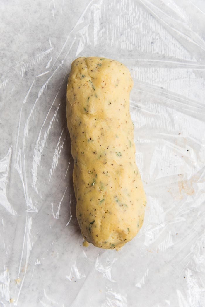 Recipe process for making thyme and cheddar cheese cookies - A cheese cookie log placed of plastic wrap.