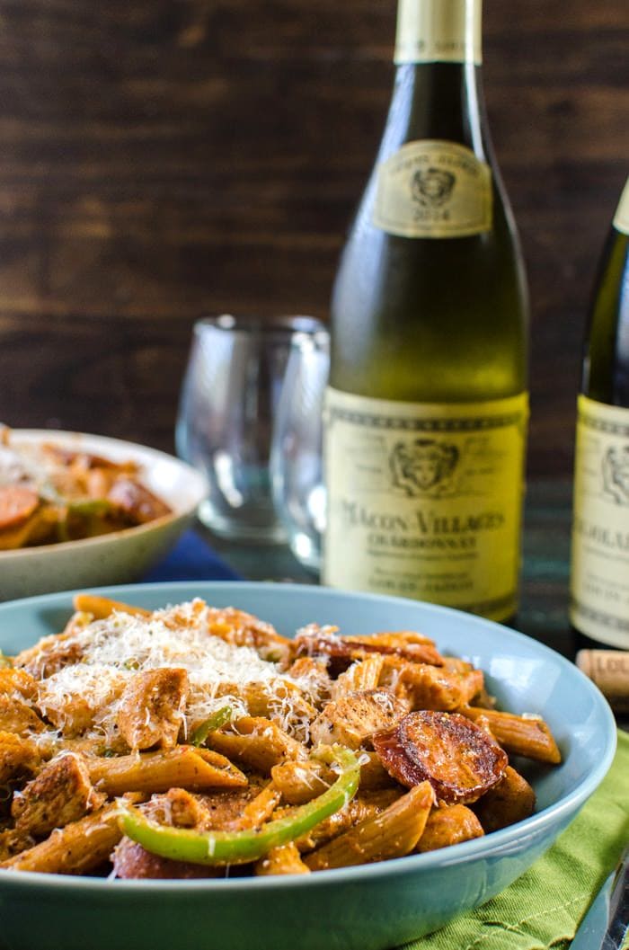 Cajun chicken and sausage pasta served on a blue plate with two wine bottles in the background.