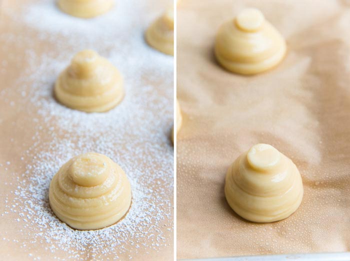 Piped choux pastry on a parchment paper lined baking tray, one dusted with confectioners sugar, the other misted with water