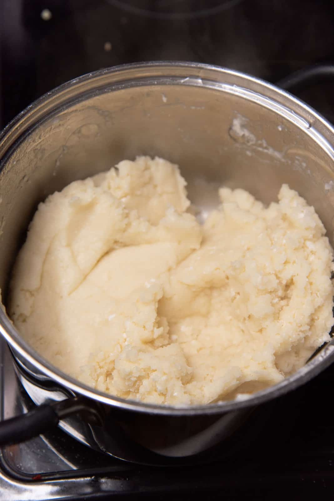 A mixture of dough inside the pot that is pale yellow, with some white dry flour spots in the dough to make churros.