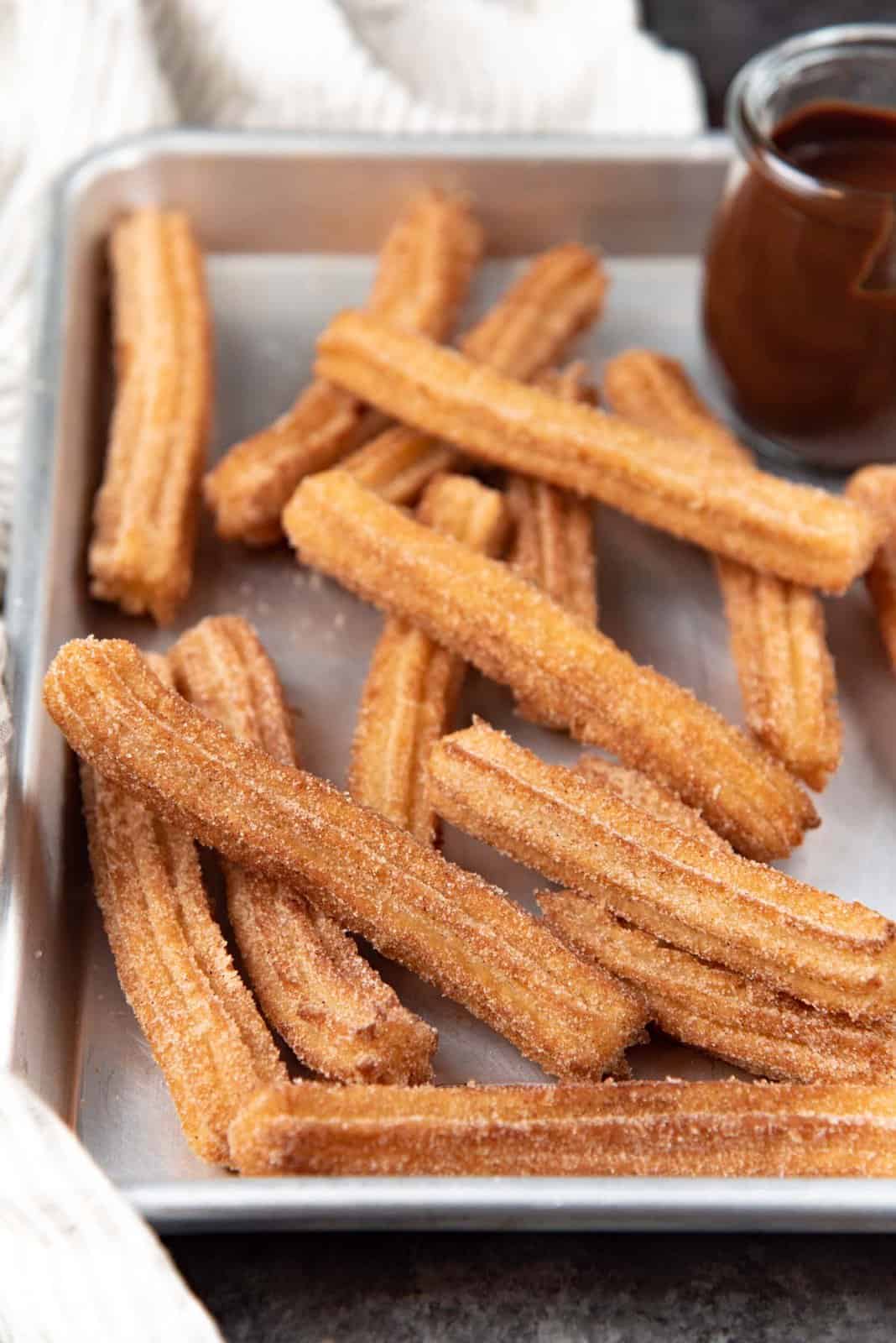 Traditional authentic churros coated in cinnamon sugar, served on a metal tray.