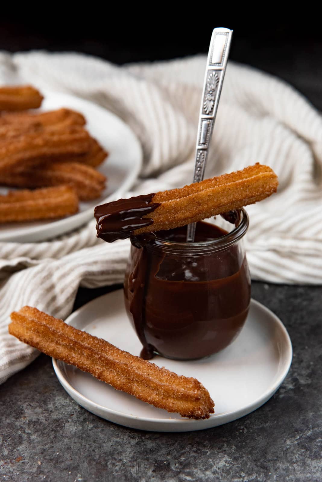 An image of cinnamon coated classic churros served with chocolate sauce in a pot, all placed on a white plate.