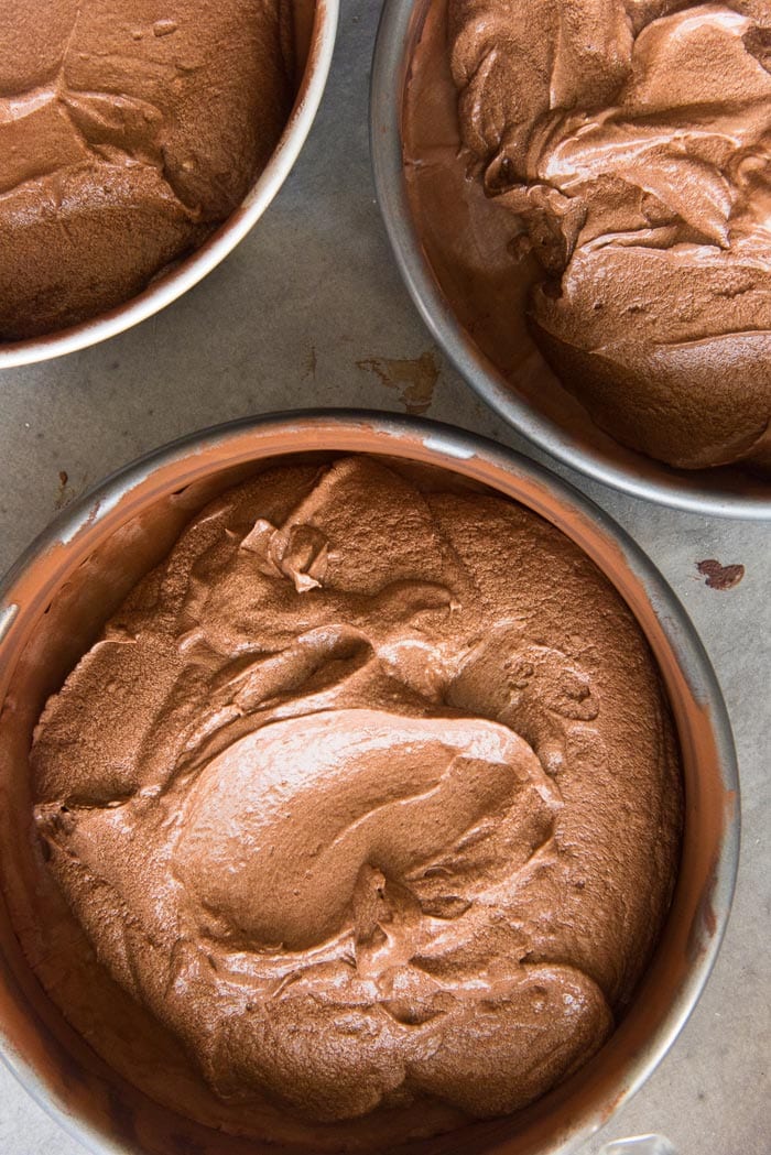 The chocolate cake batter divided into the prepared cake pans.