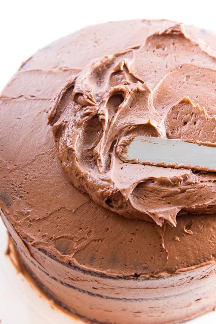 An offset spatula swirling buttercream onto the top of the chocolate layer cake. Swirl the chocolate buttercream frosting onto the crumb coating that has been "set". The crumb coating will prevent any cake crumbs getting on the final frosting layer.