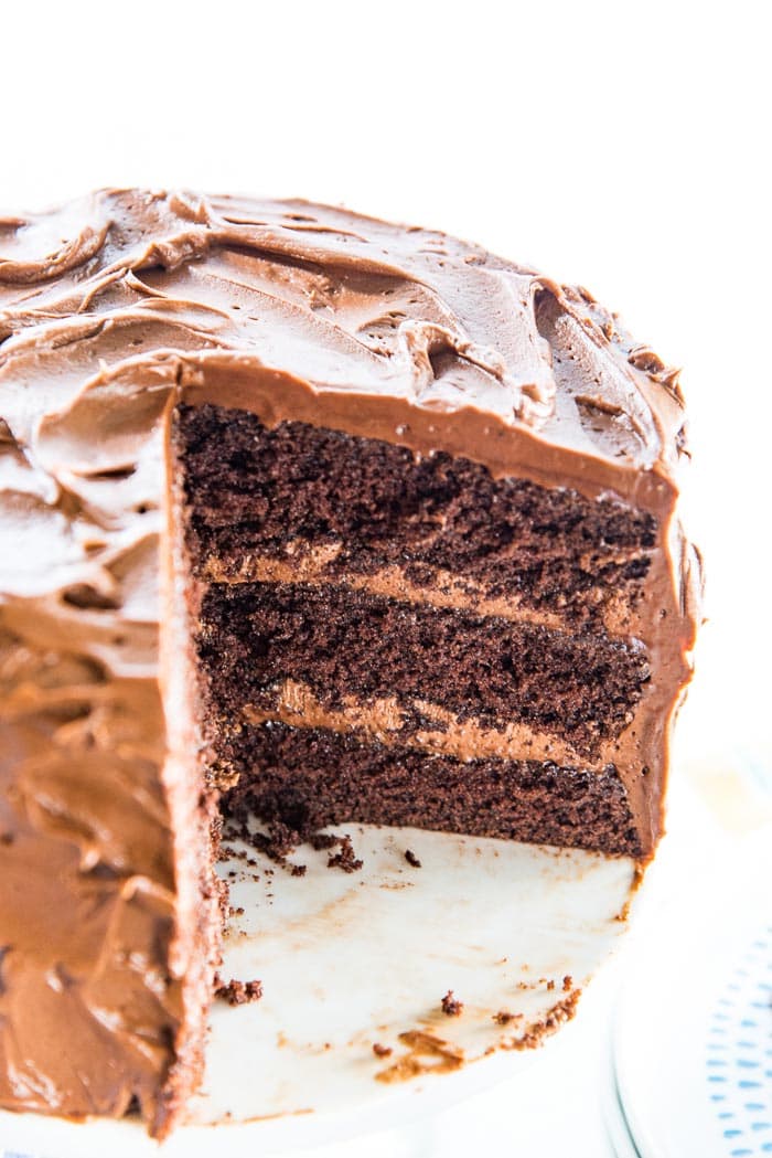 A half cut chocolate cake, showing the three chocolatey, airy, chocolate cake layers and the billowy, creamy chocolate frosting.