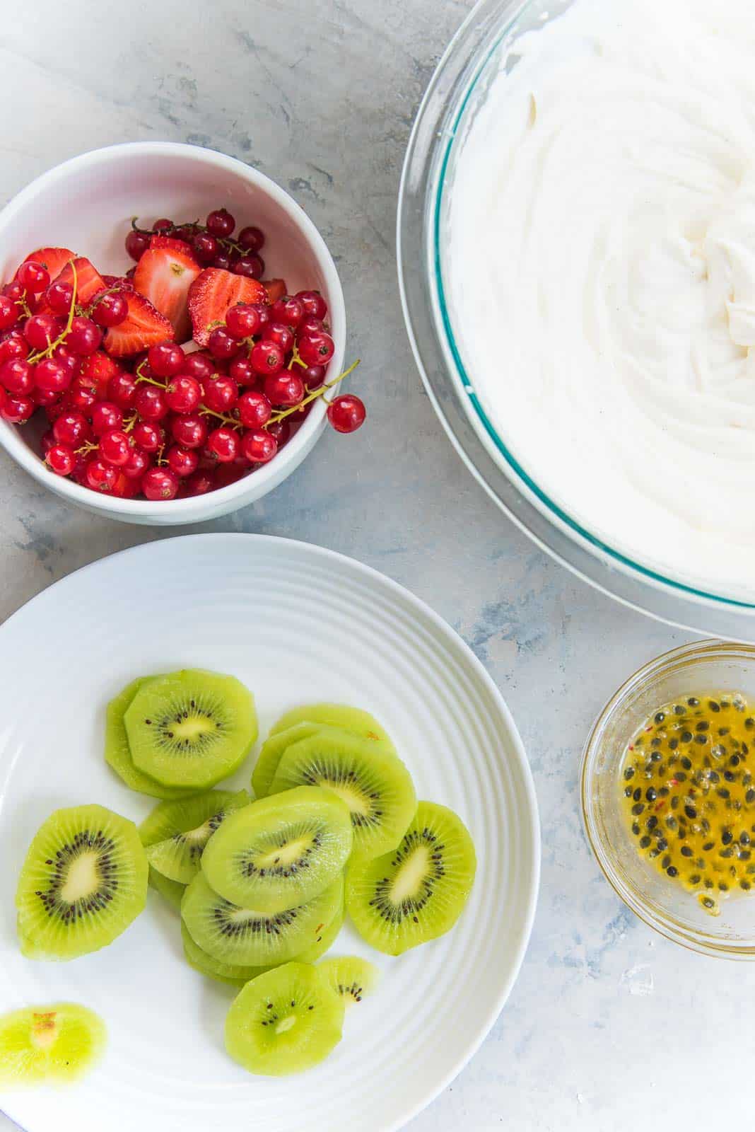 An overhead view of toppings for a classic pavlova - whipped cream, and sliced and chopped fruits