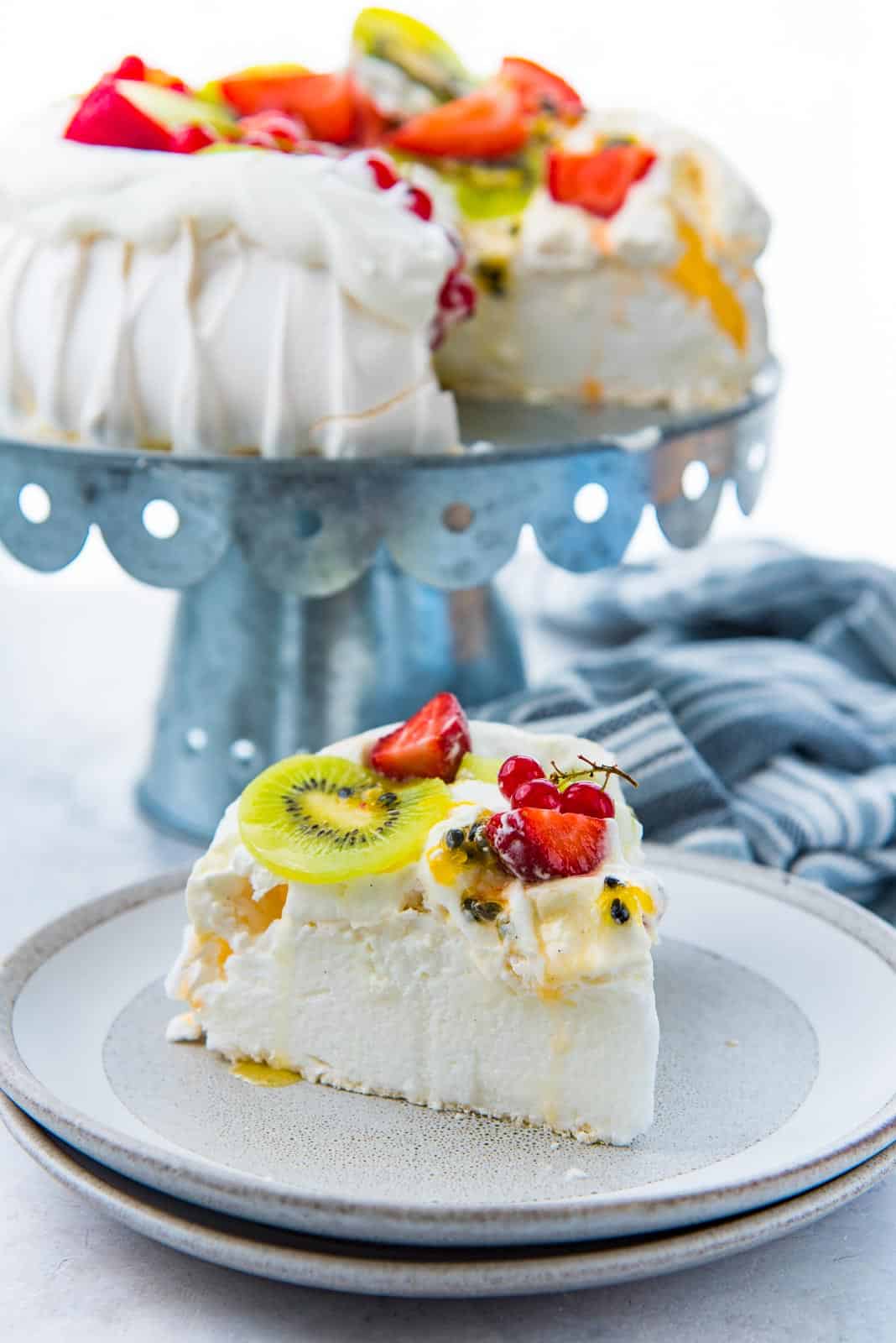 A slice of pavlova on a grey plate, topped with cream and kiwifruit, strawberries and passion fruit