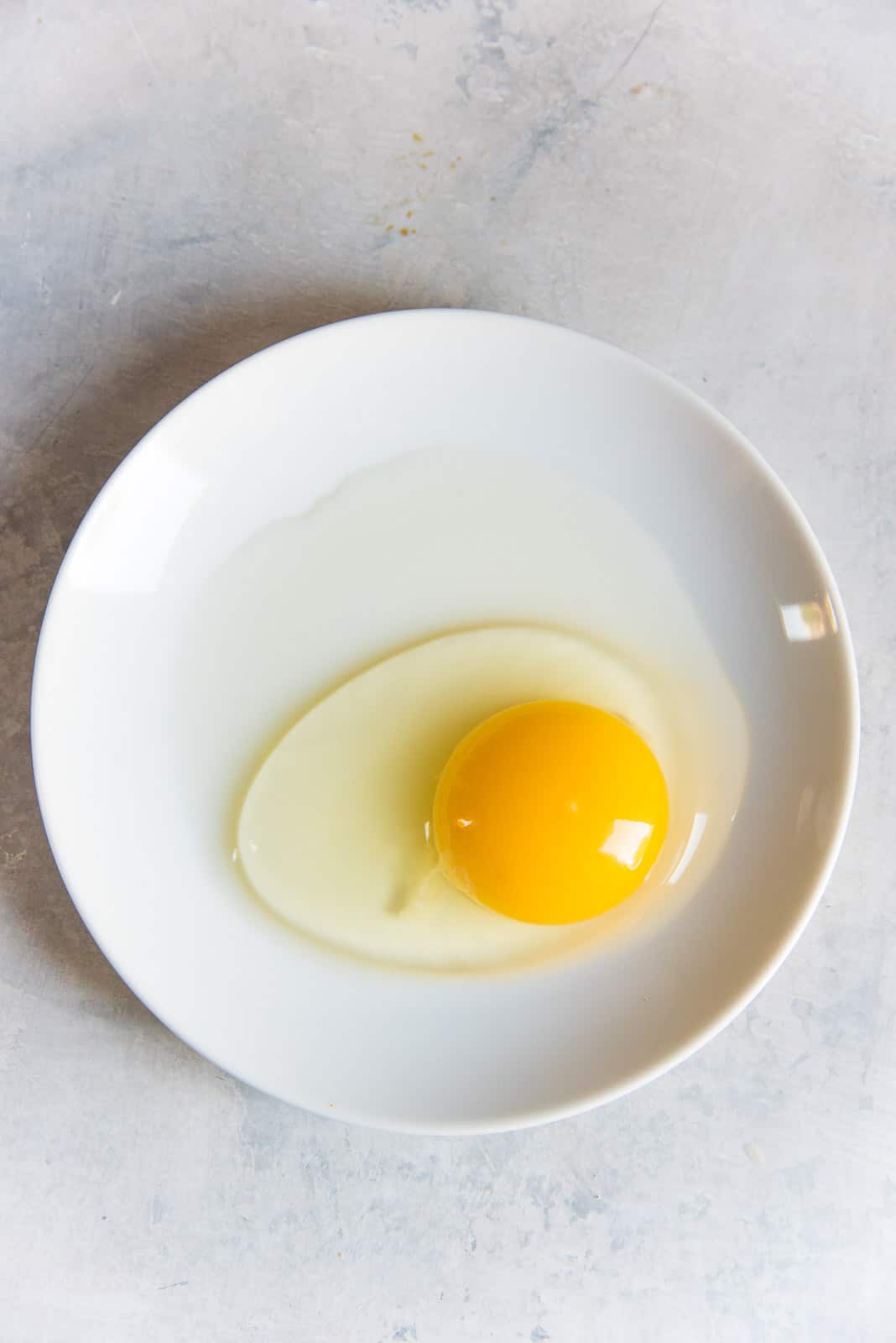 A fresh egg on a white plate, showing the right and thick egg white around the yolk.