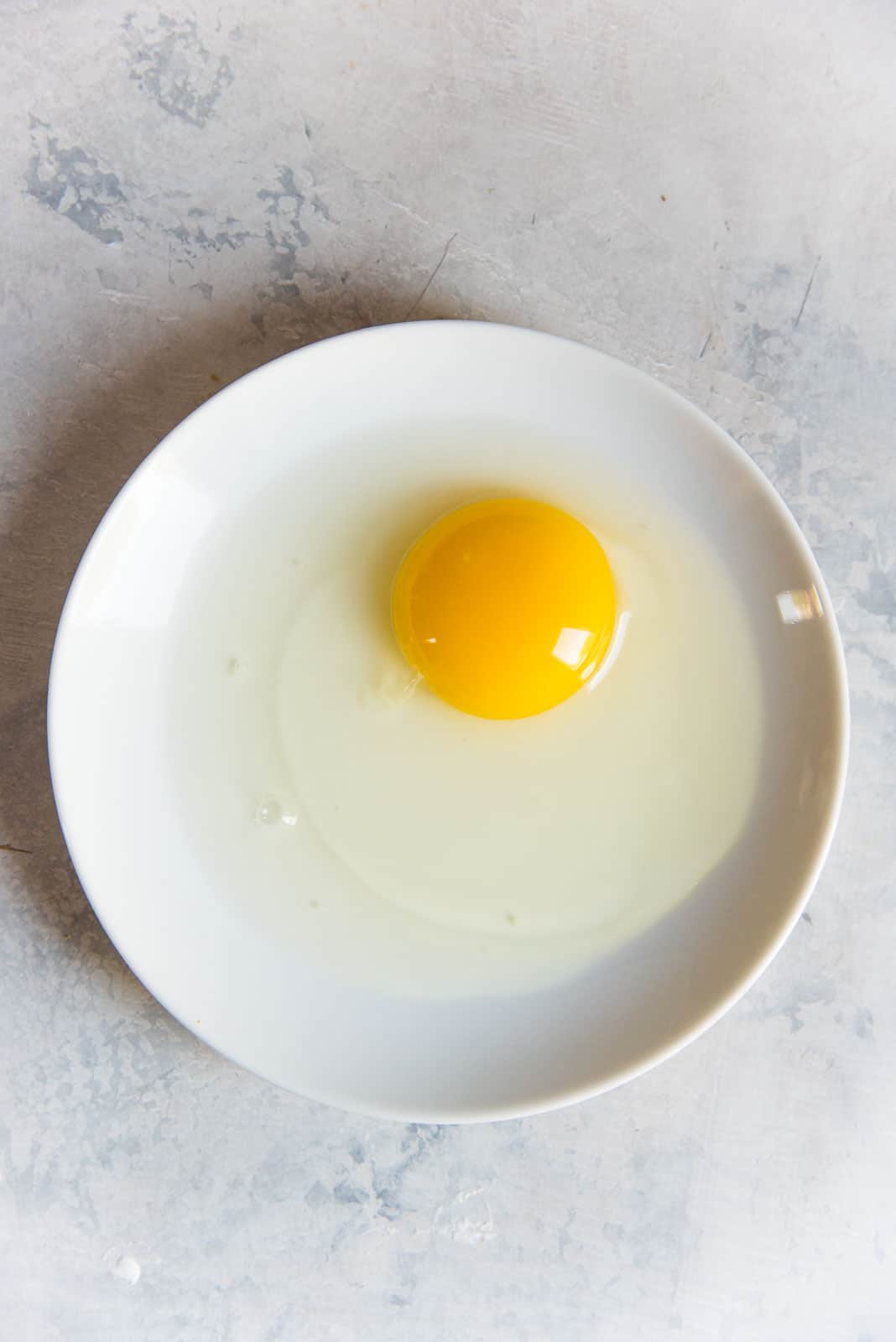 An old egg on a white plate, showing the loose and runny egg white around the yolk