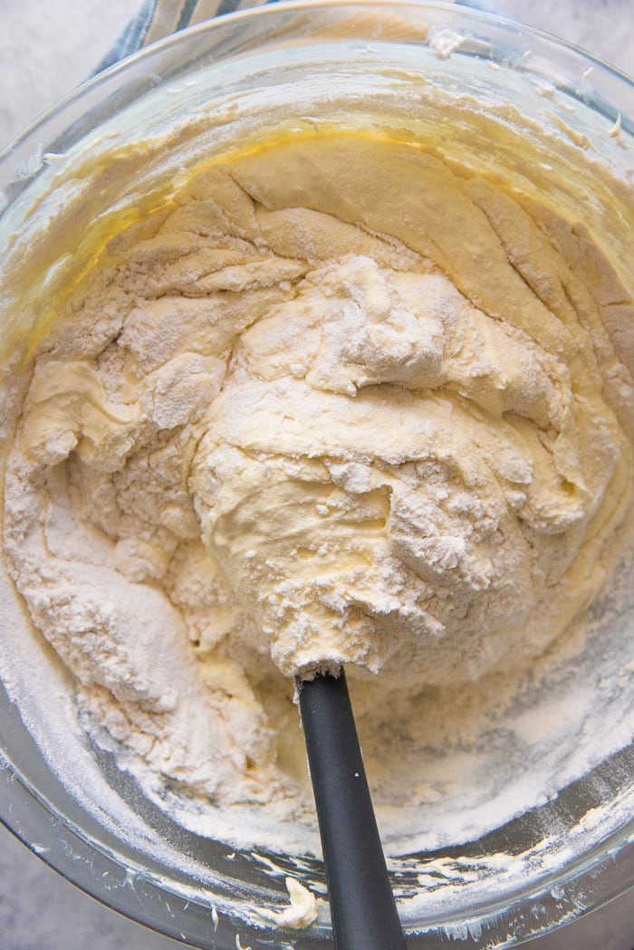 A spatula folding in the flour into the cake batter. Fold the flour in carefully without overworking the gluten. 