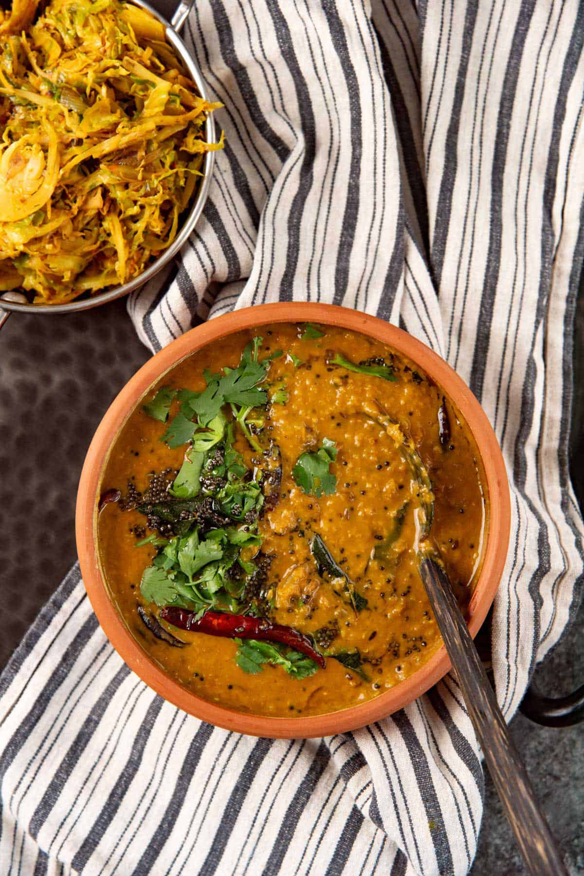 Overhead view of spiced dhal curry in a clay bowl, with a coconut spoon for serving.