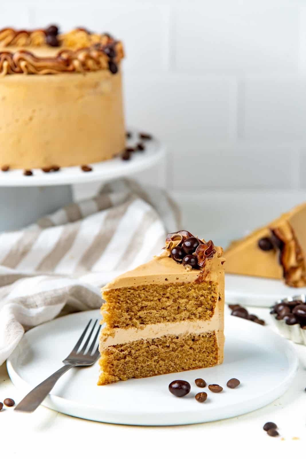 A slice of the coffee layer cake on a white plate with the whole cake in the background