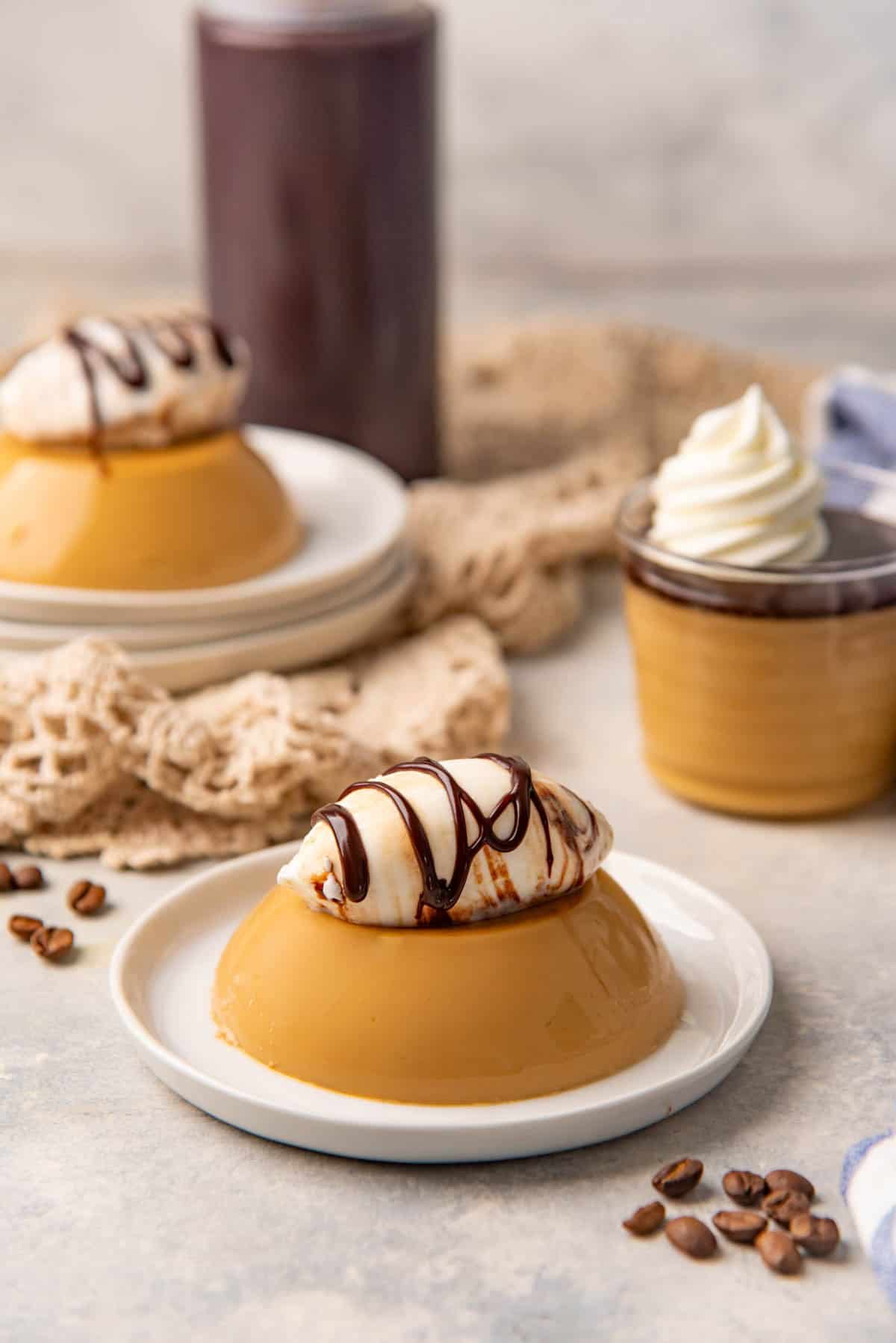 Coffee panna cotta on a small plate topped with whipped cream and a drizzle of hot fudge sauce.