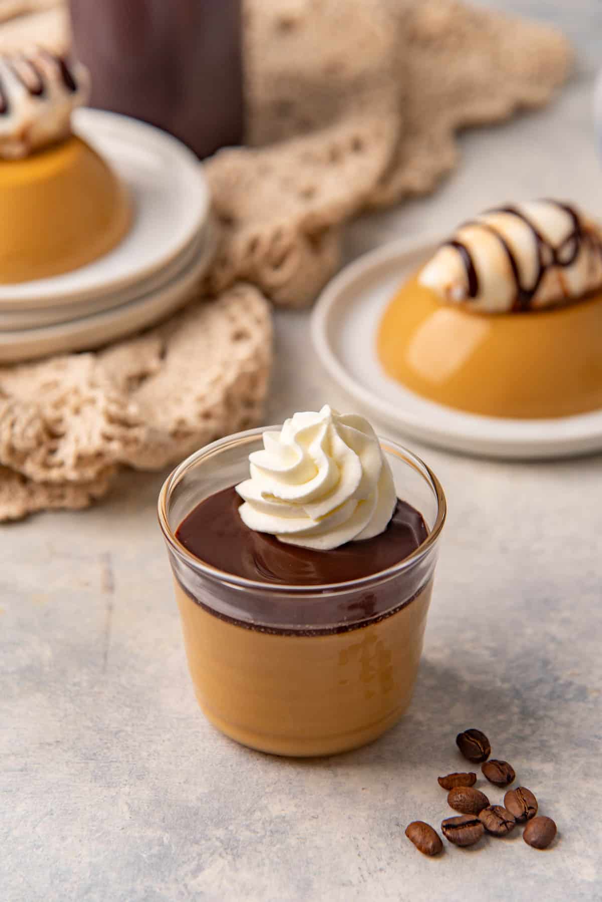Coffee panna cotta in a glass topped with a layer of chocolate sauce and dollop of whipped cream.