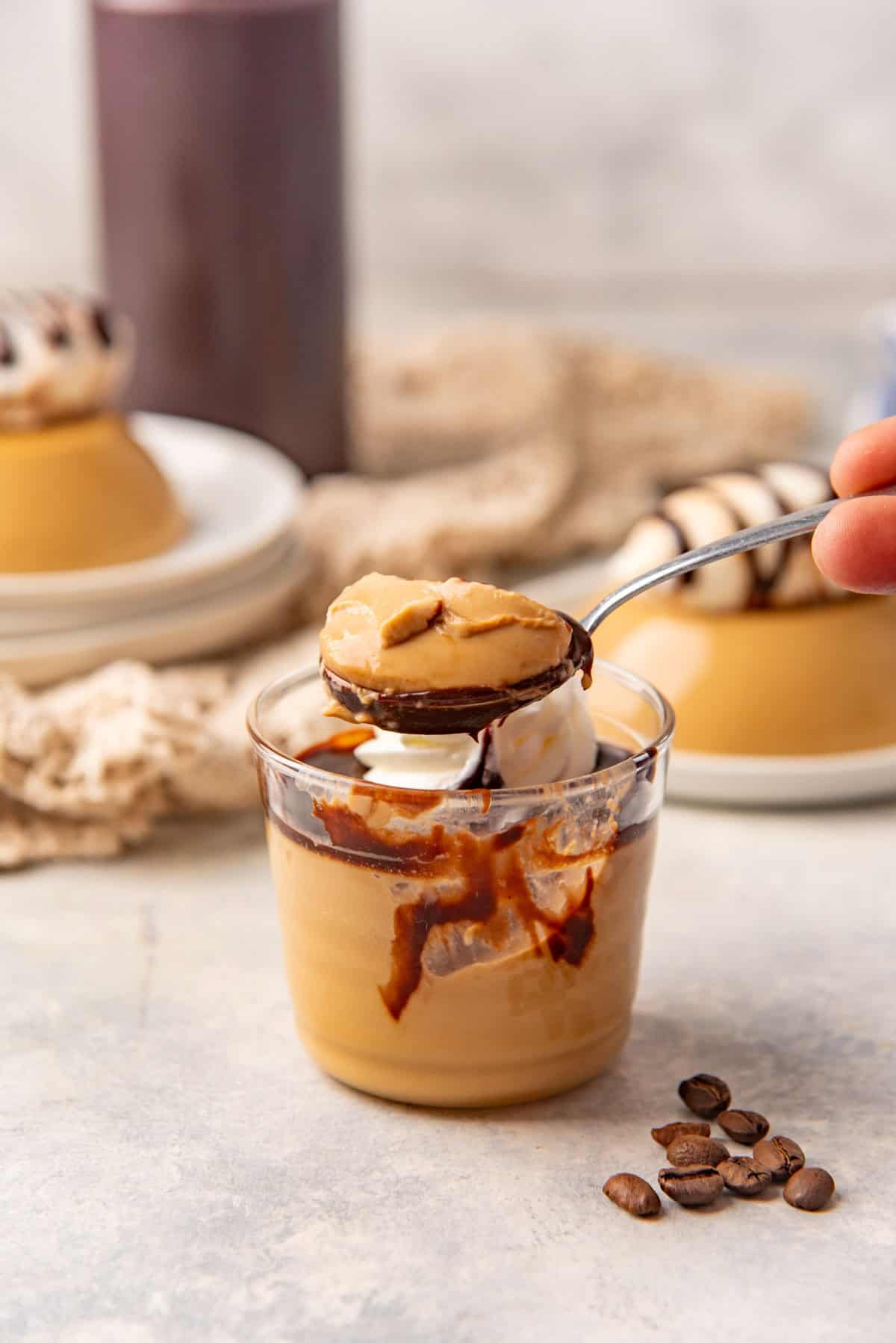 A spoon holding up a scoop of creamy coffee panna cotta with coffee beans next to it.