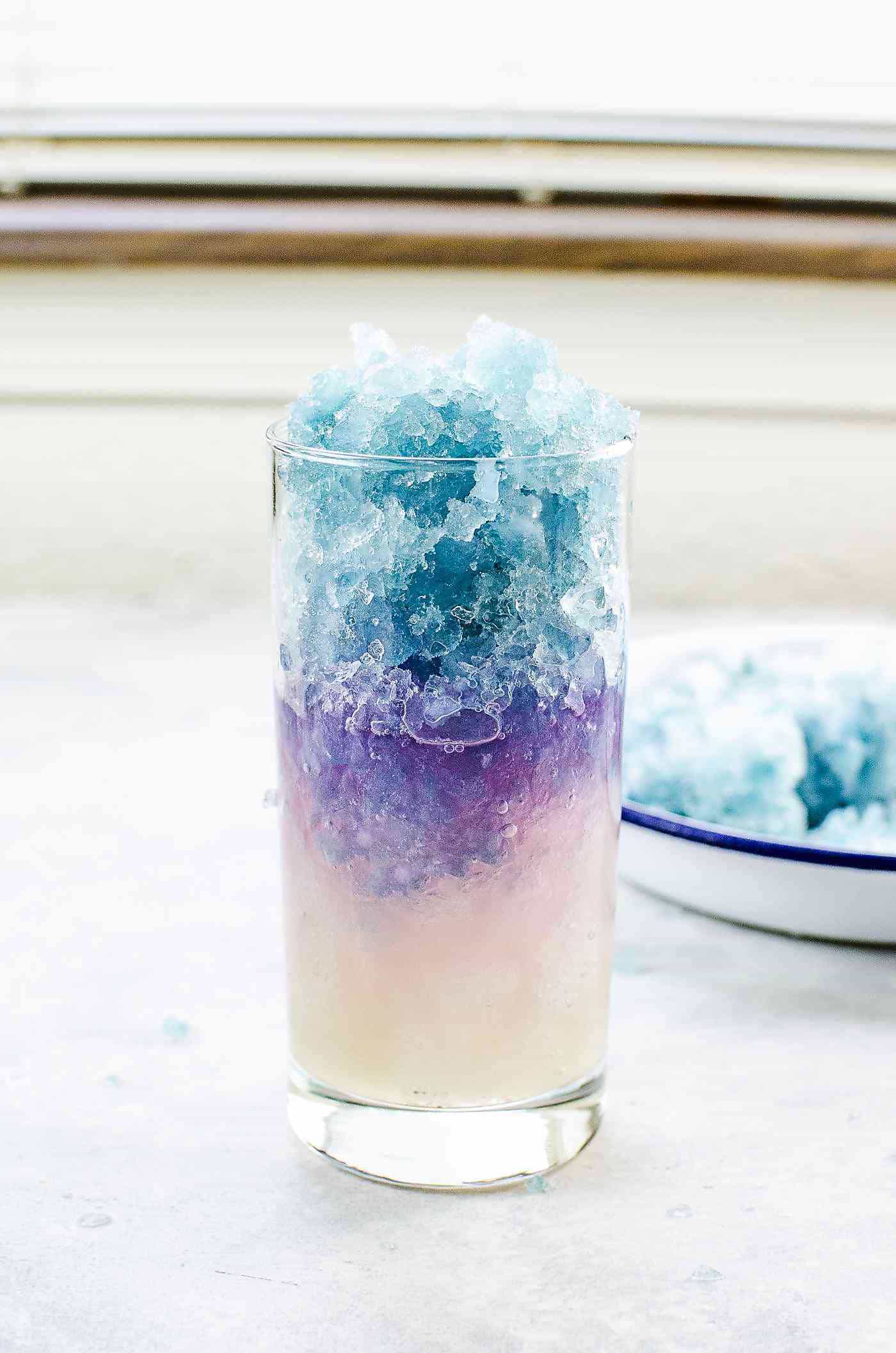 Pouring lemon syrup into a glass with crushed regular ice and blue ice and blue ice turning purple. 