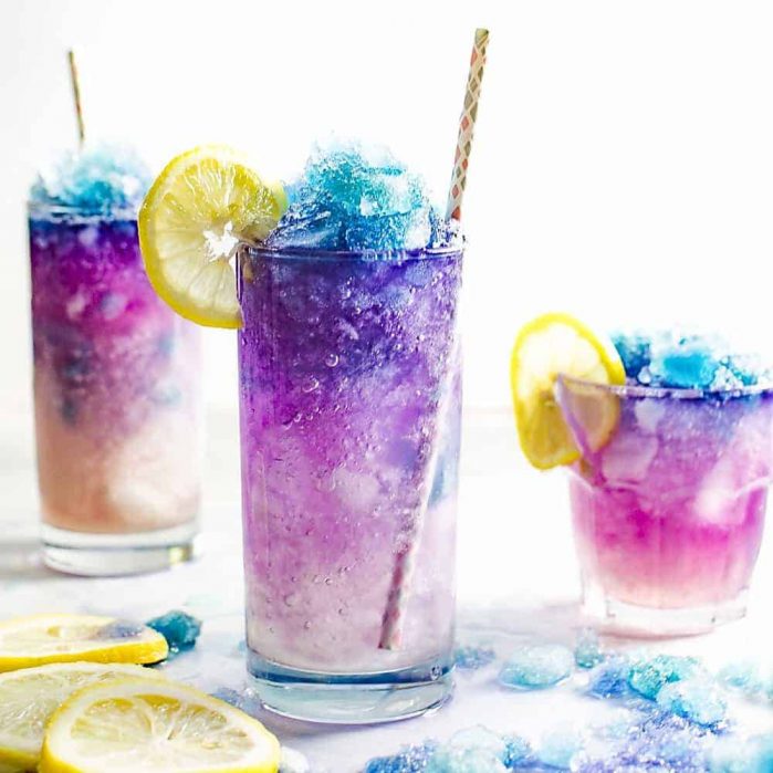 Three glasses of colorful galaxy lemonade with straws and lemon slices on the glass rim.