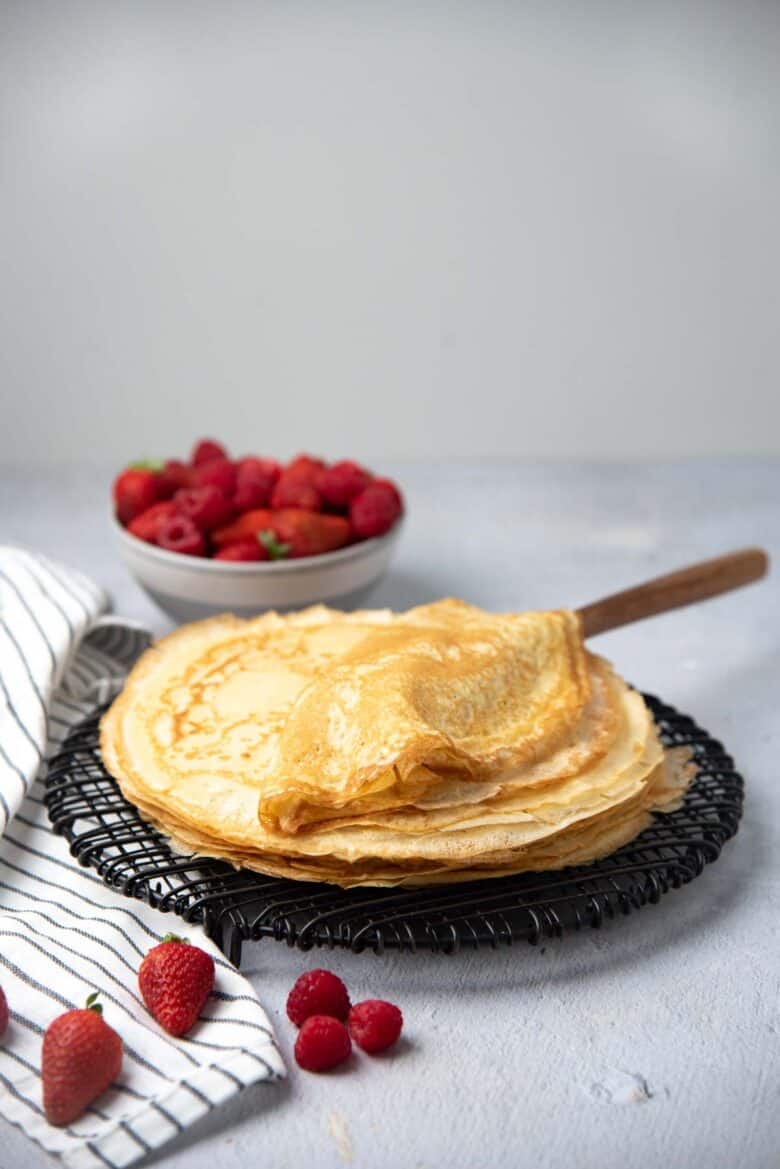 A stack of freshly made crepes on a black wire rack
