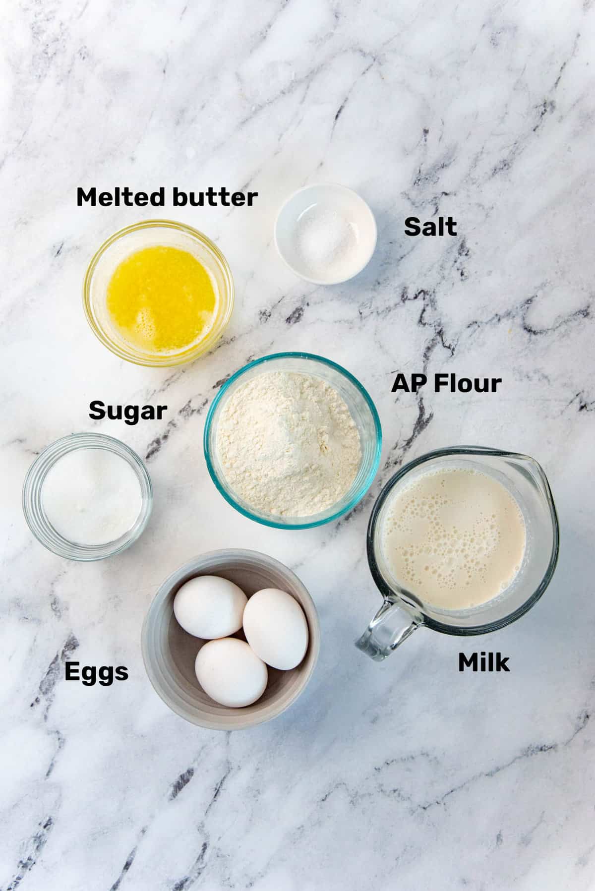 Overhead view of ingredients needed for French crepes recipe, in separate bowls.