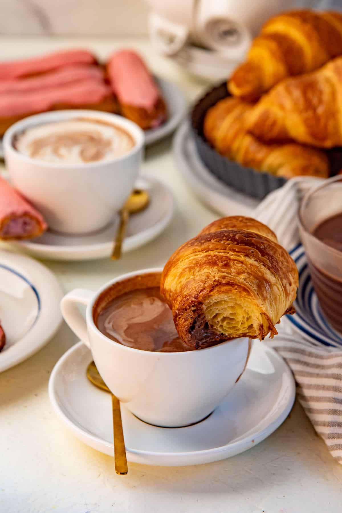 A half eaten flaky croissant placed on top of a mug with thick, creamy hot chocolate.